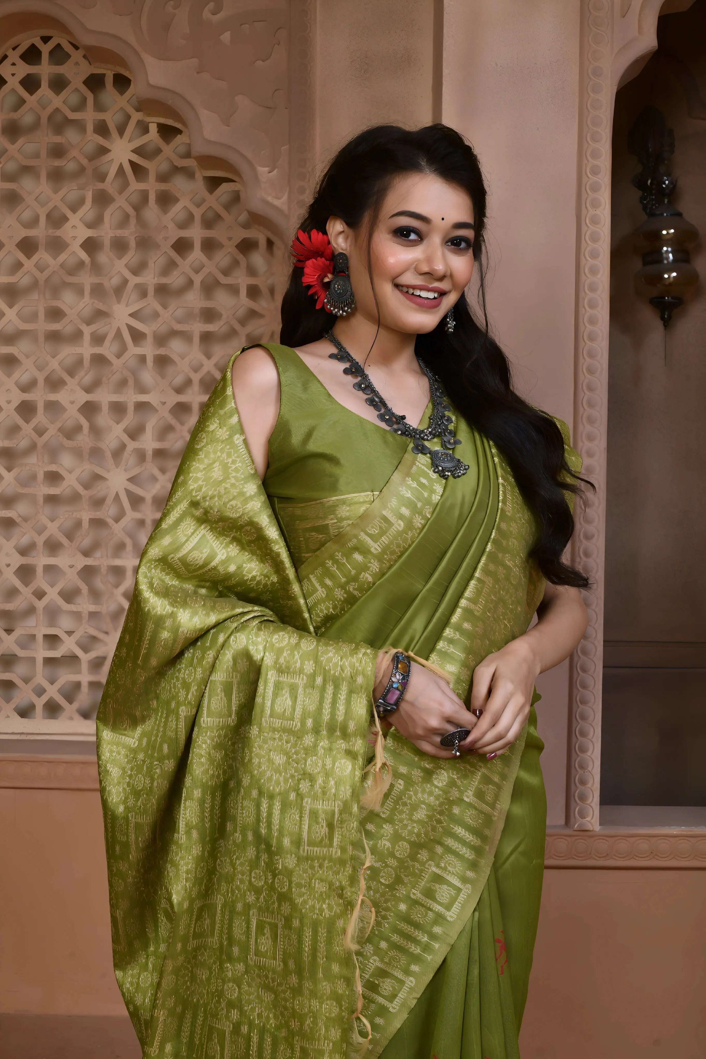 A woman models a striking Pista Green Banglori Raw Silk Saree. The pallu and border feature dense, tone-on-tone Kalamkari-style weaving in gold Zari. She wears a sleeveless green blouse and heavy oxidized silver or dark gemstone jewelry, posing in an ornate, traditional setting.